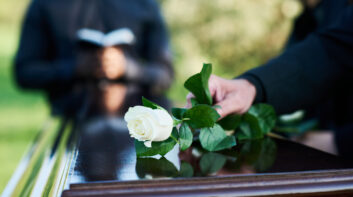 Fresh white rose being put by woman in mourning attire on closed coffin lid