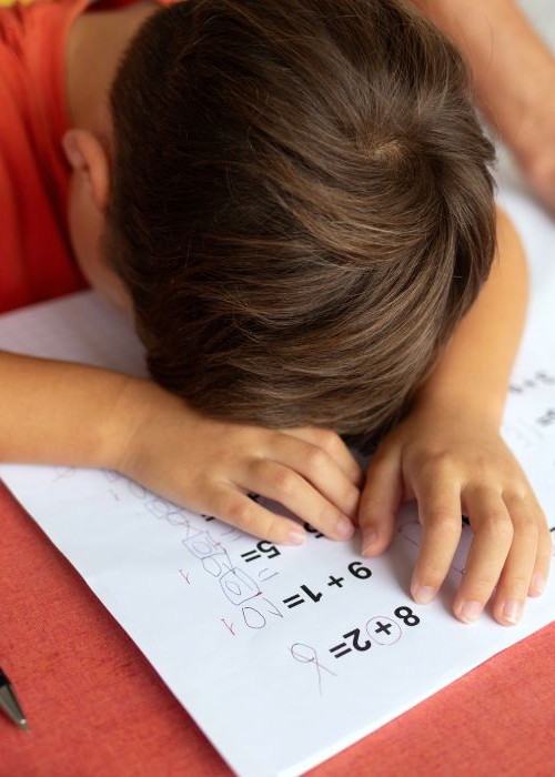 Elementary school student sitting at desk with his head down struggling with math