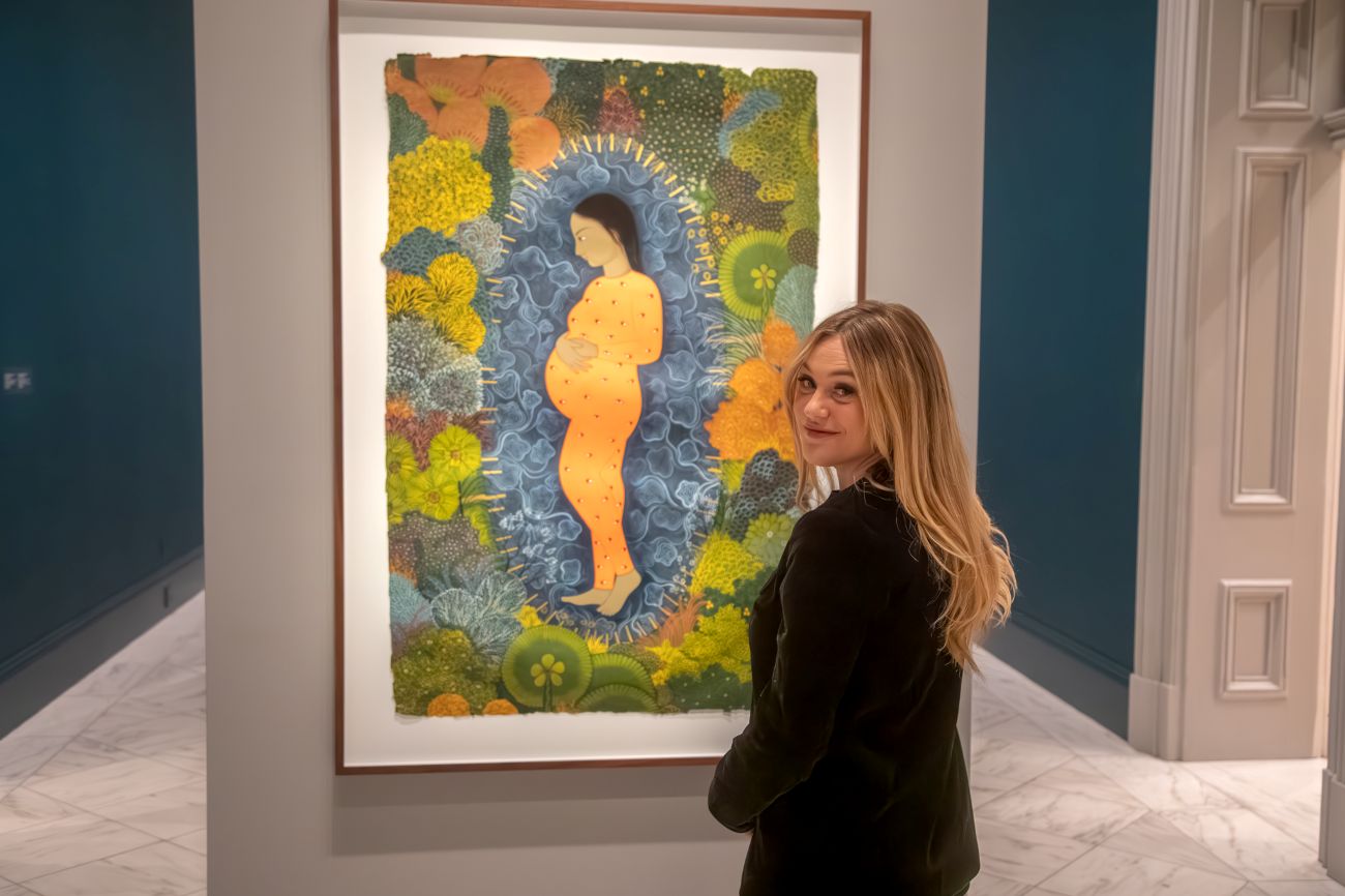 Isabel Brown looking over her shoulder in front of a portrait of a pregnant woman
