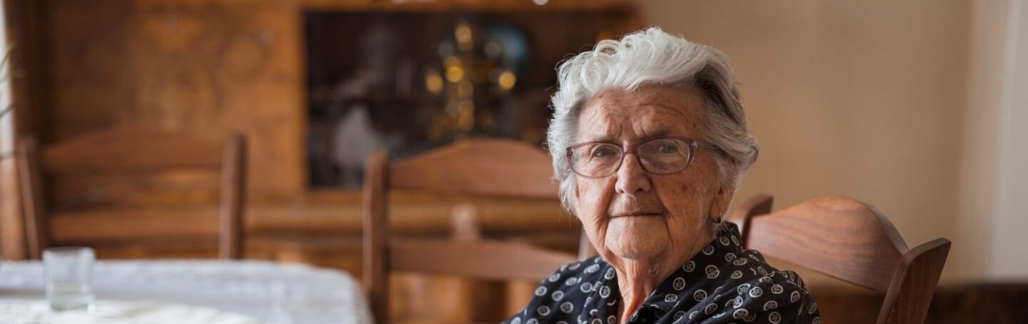 Elderly woman sitting at her kitchen table header