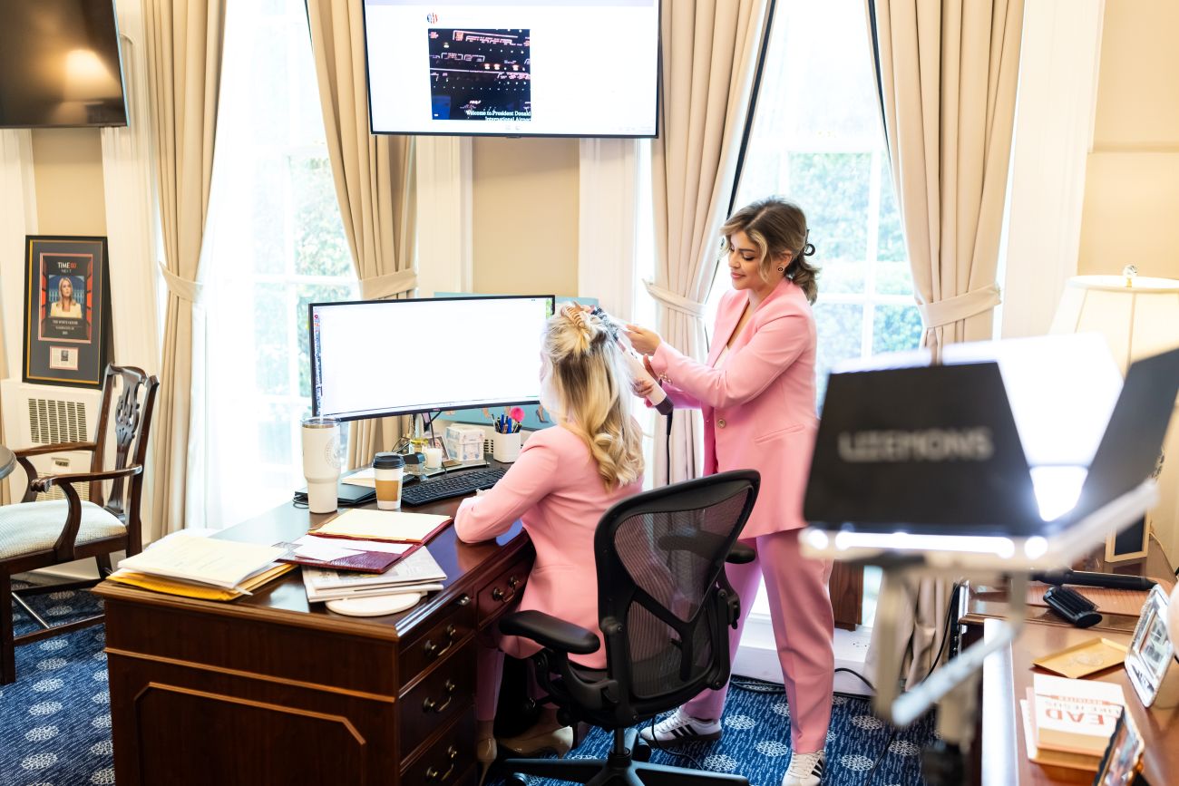 Danielle styling Leavitt's hair while Leavitt works on her computer